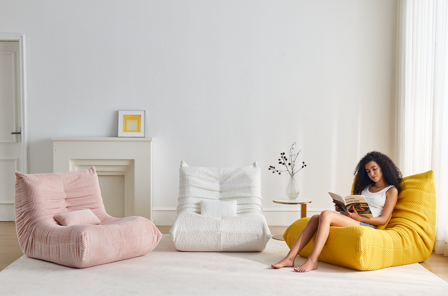Woman reading a book on a yellow bean bag chair in a modern living room with pink and white bean bag chairs.