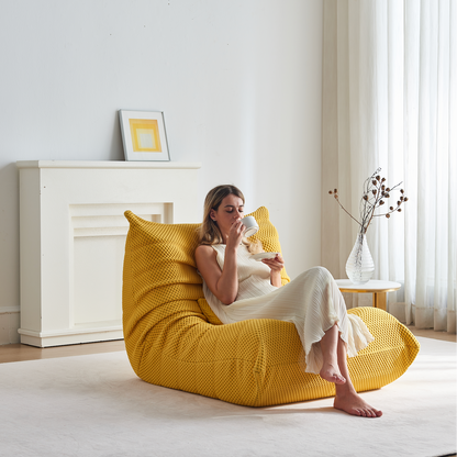Woman sitting on Zoovee's yellow airpore bean bag chair in a bright room enjoying her coffee.
