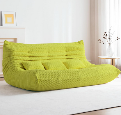 Green bean bag floor sofa three seater in a room with a white wall and small table.