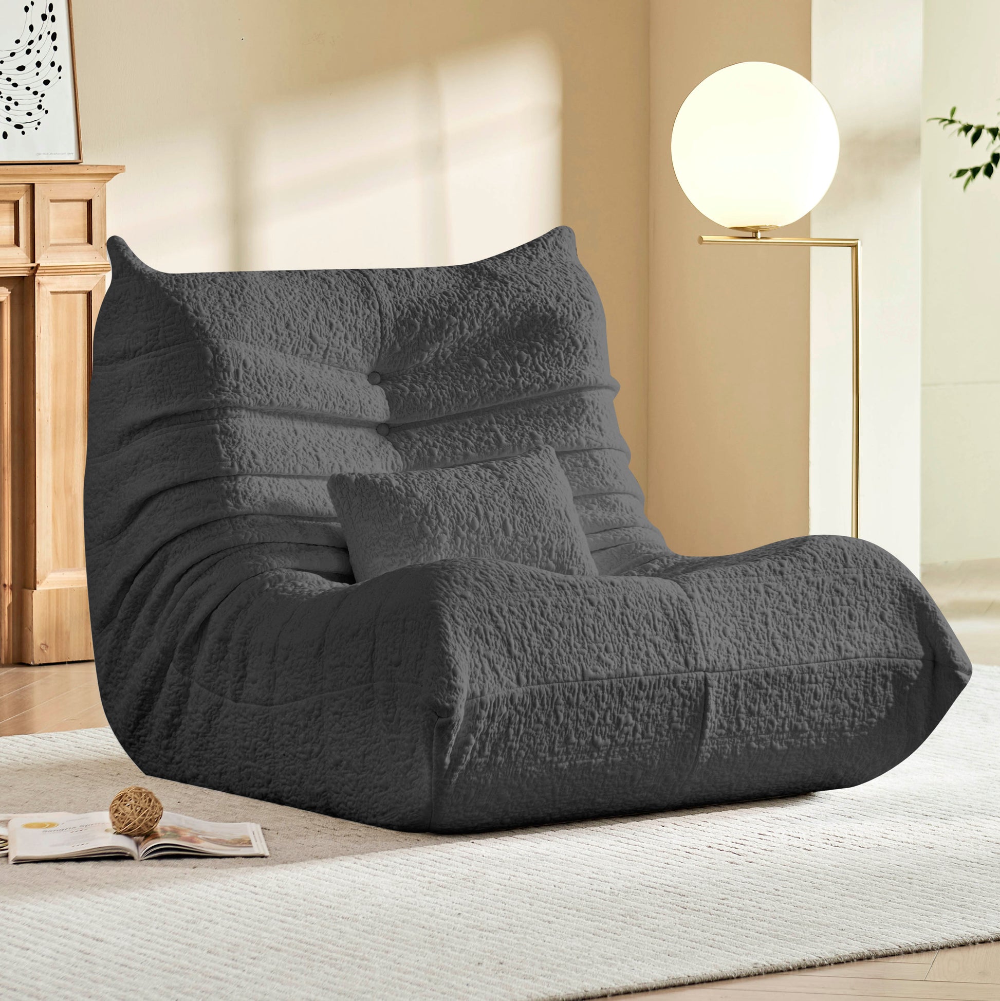 Gray textured bean bag chair in a living room setting with a lamp and book.