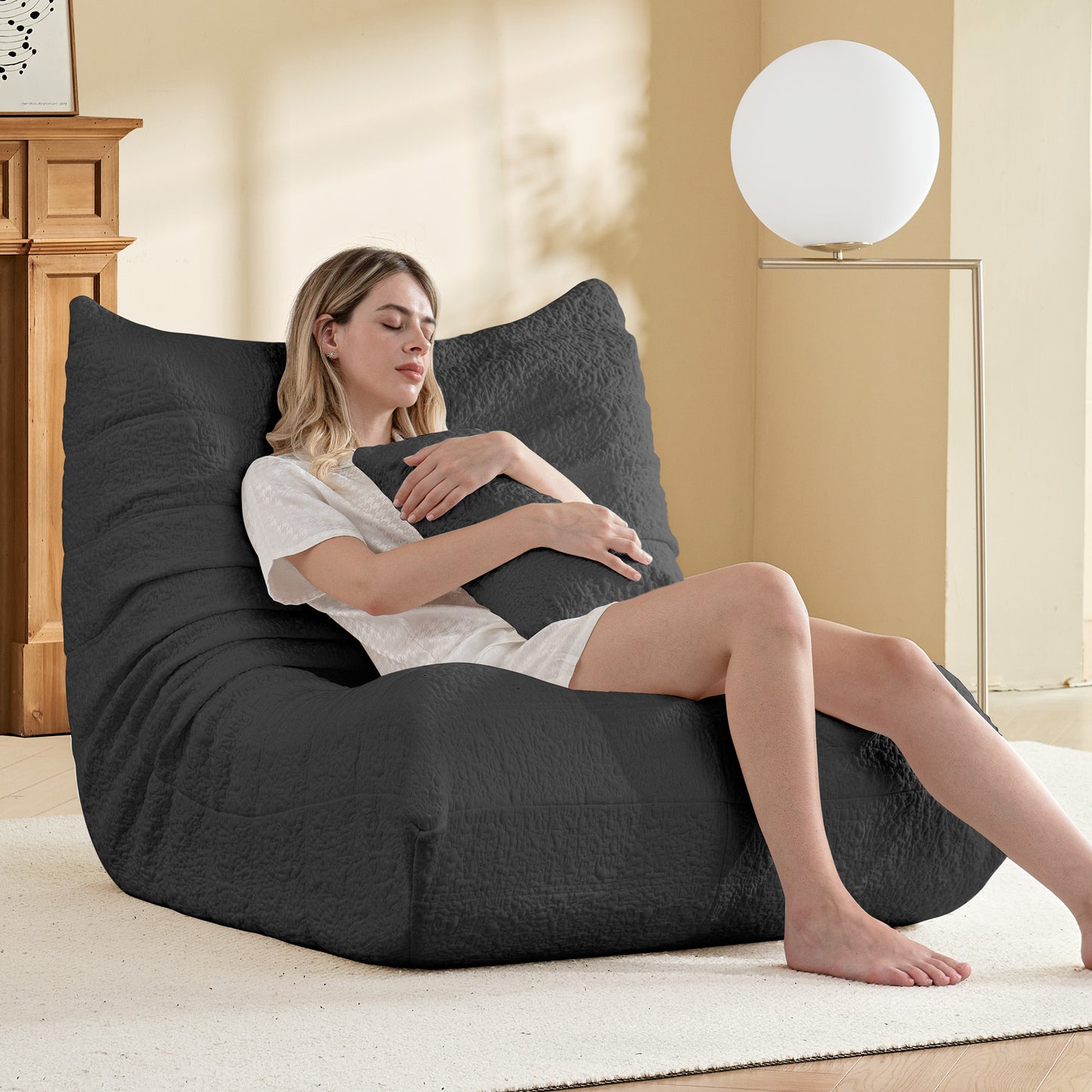 Woman sitting on a large gray bean bag chair in a cozy living room.