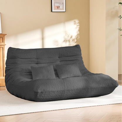 Gray bean bag chair loveseat in a room with a wooden cabinet and framed pictures on the wall.