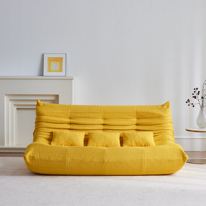 Yellow bean bag floor sofa 3 seater in a minimalistic room with a white wall and wooden floor.