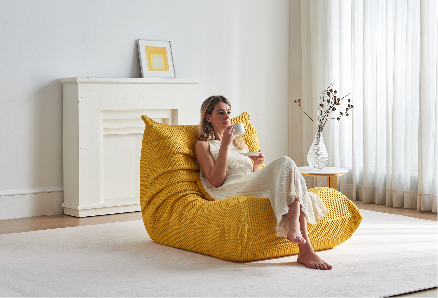 Woman sitting on Zoovee's yellow airpore bean bag chair drinking coffee in a bright room.
