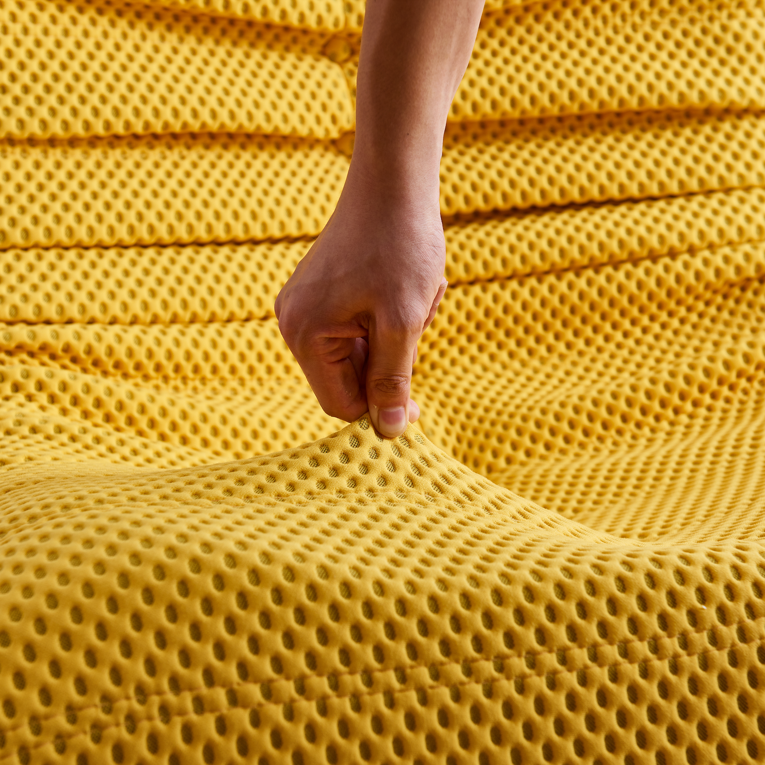 Hand touching a textured yellow airpore fabric surface