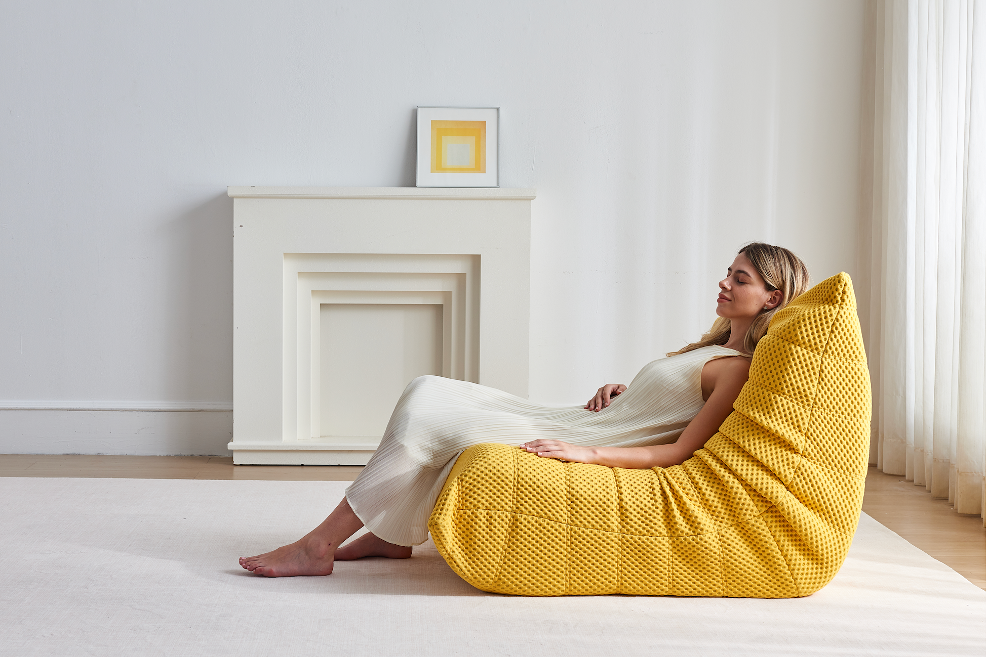 Woman resting on Zoovee's yellow airpore bean bag chair in a minimalistic room.