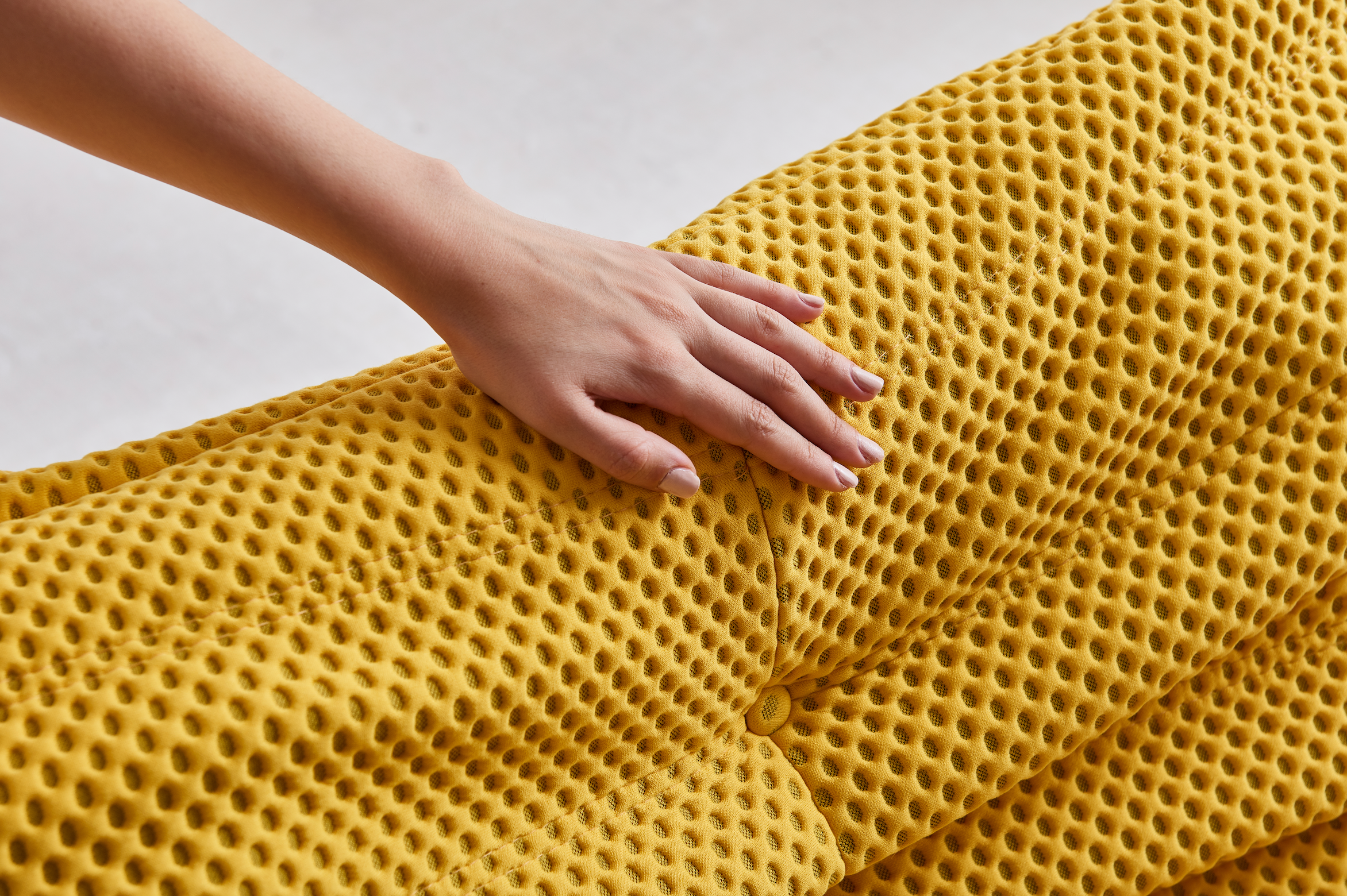 Hand touching a yellow airpore honeycomb-patterned fabric
