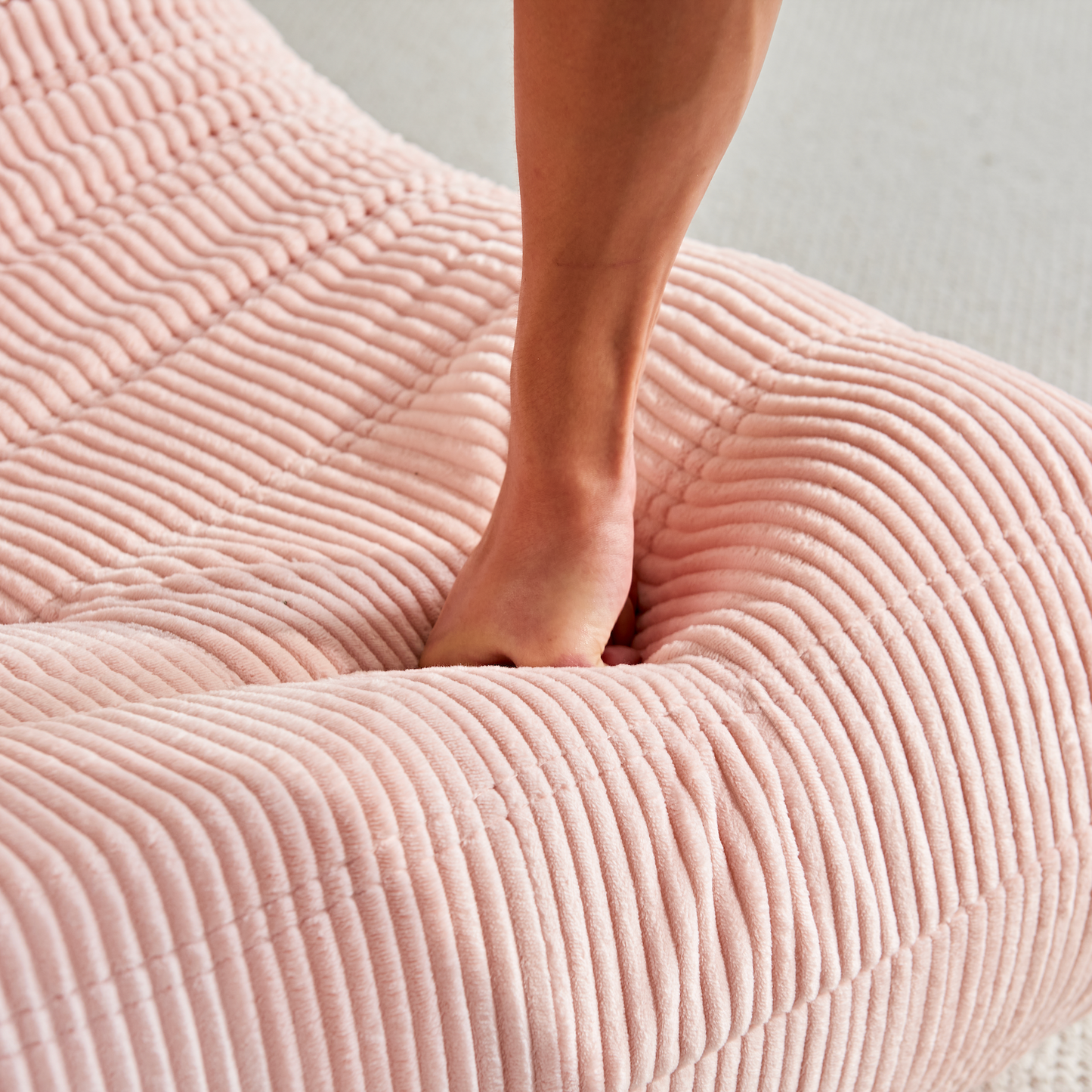 Person's fist punching onto Zoovee's pink corduroy bean bag chair on a light background